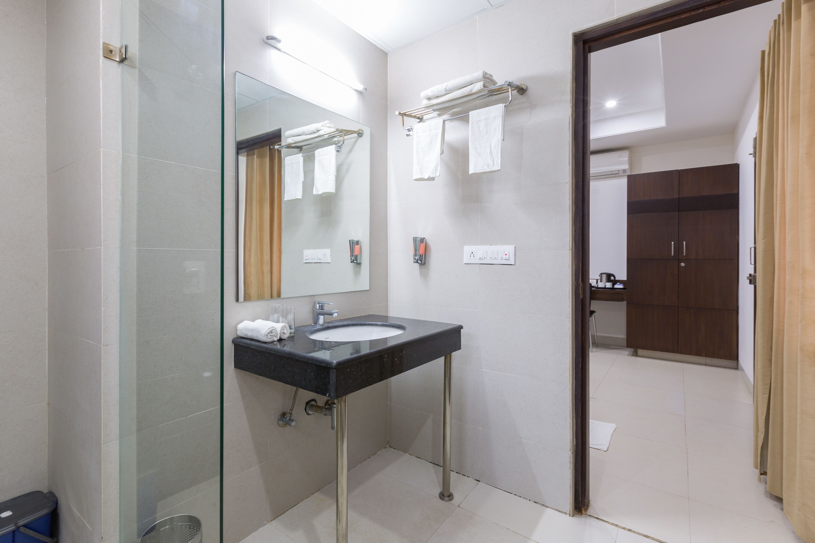 A modern bathroom with a glass shower enclosure, a black sink with chrome legs, and a mirror above the sink.