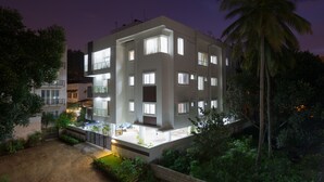 Un edificio de varios pisos con balcones y ventanas, rodeado de vegetación y palmeras.