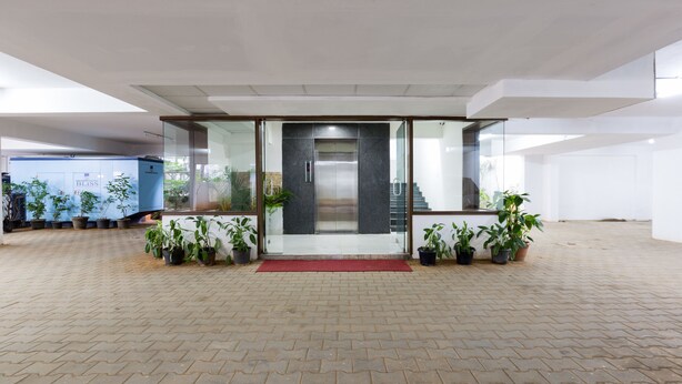 Entrada de un edificio moderno con puerta de vidrio, plantas en macetas y un felpudo rojo.