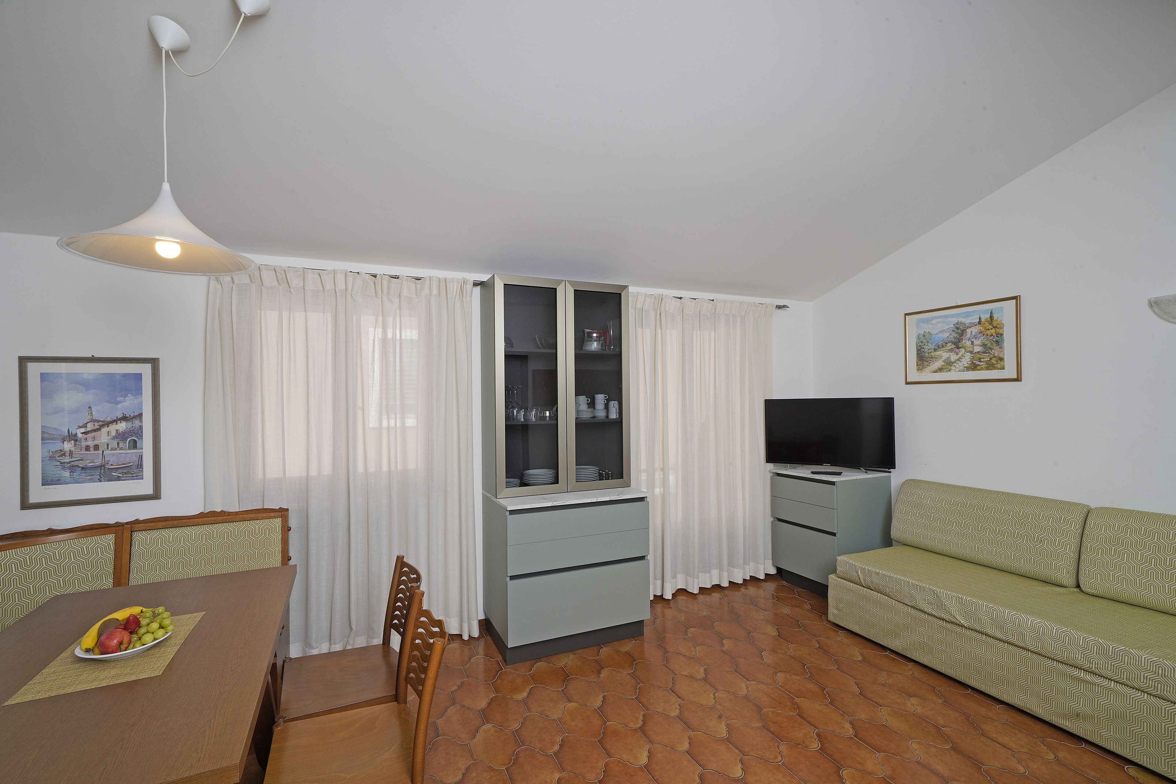 Una sala de estar con un sofá, una mesa de comedor con sillas, un aparador y una televisión.