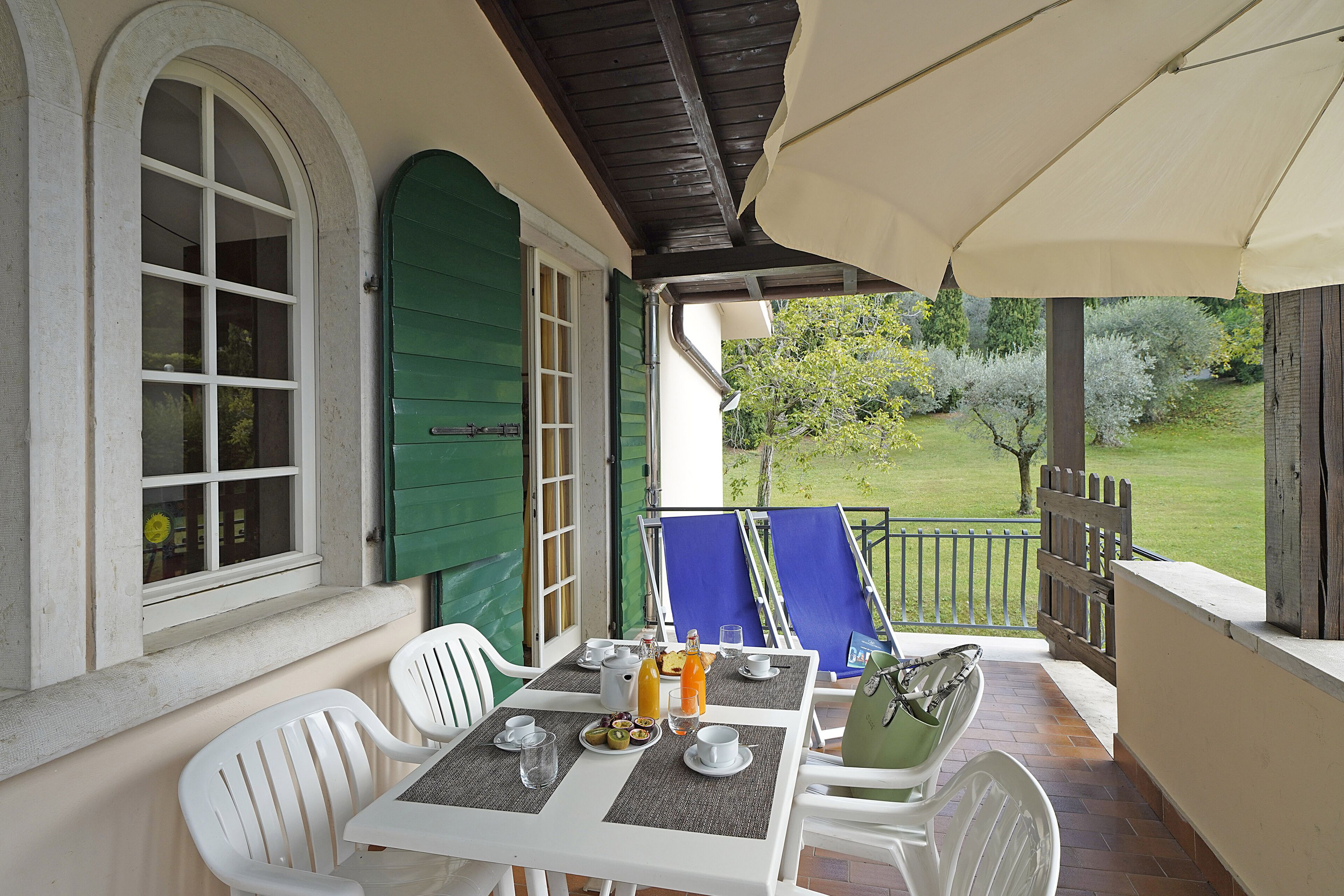 Une terrasse couverte avec une table mise pour le petit-déjeuner, comprenant des assiettes, des tasses et une bouteille de jus d’orange.