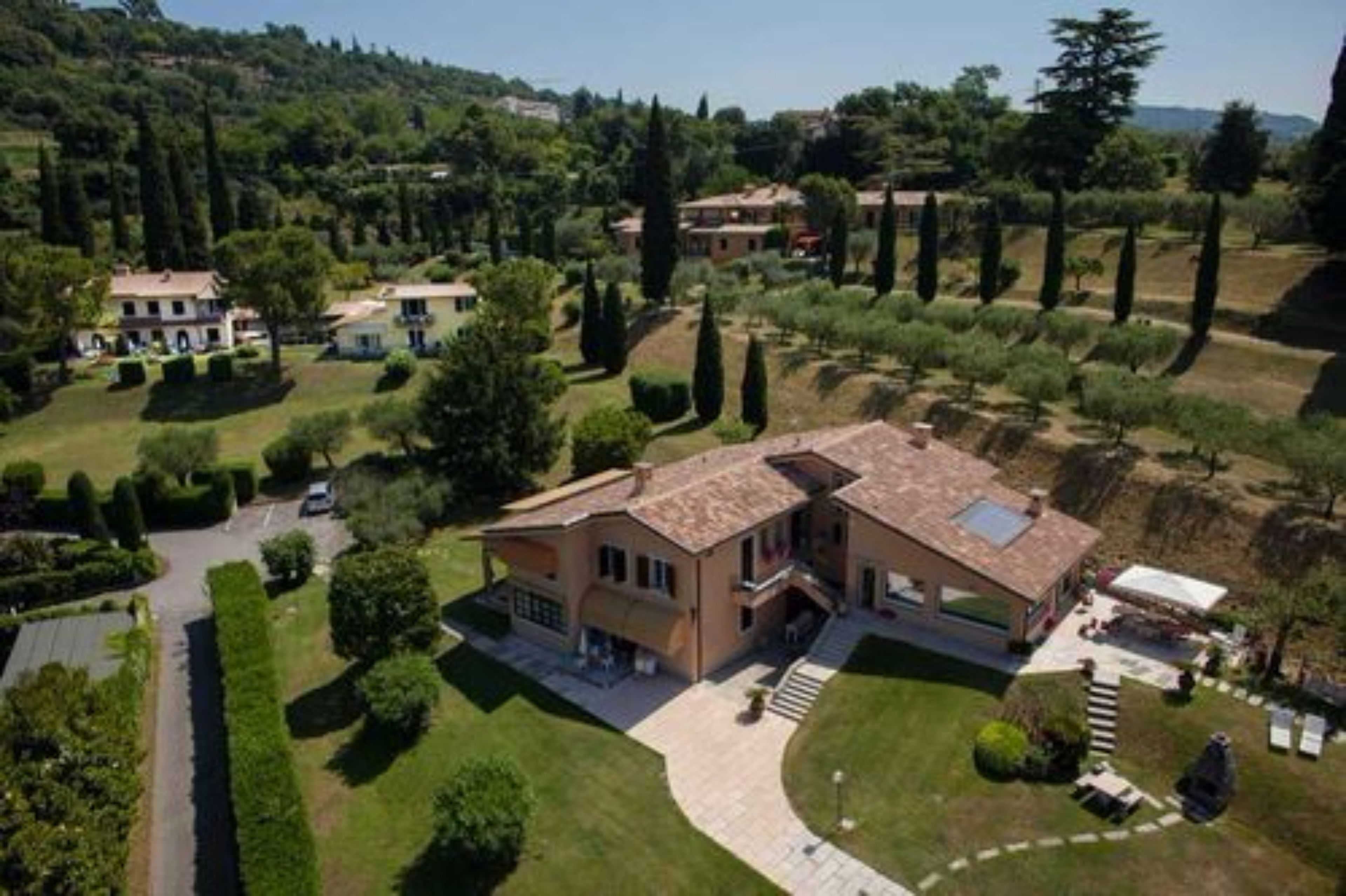 A large, two-story house with a tiled roof, surrounded by well-maintained gardens and tall trees.