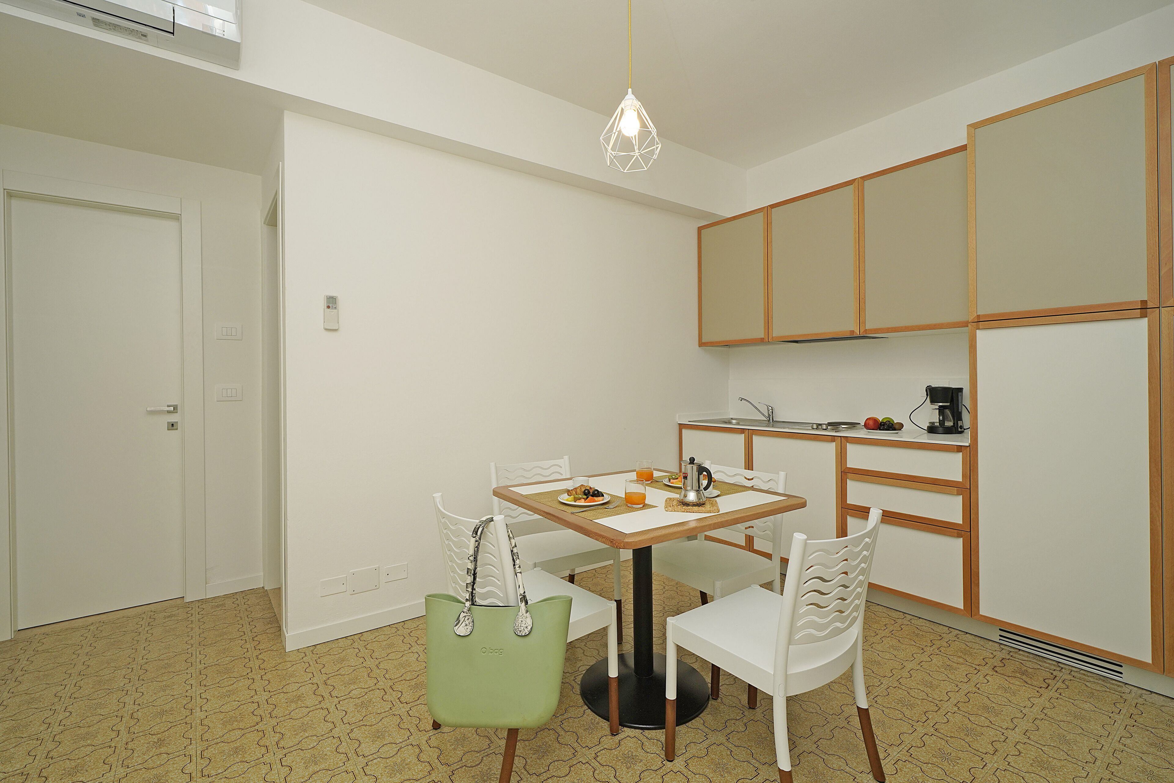 A compact kitchen with a dining table and chairs, a hanging light fixture, and wooden cabinets.