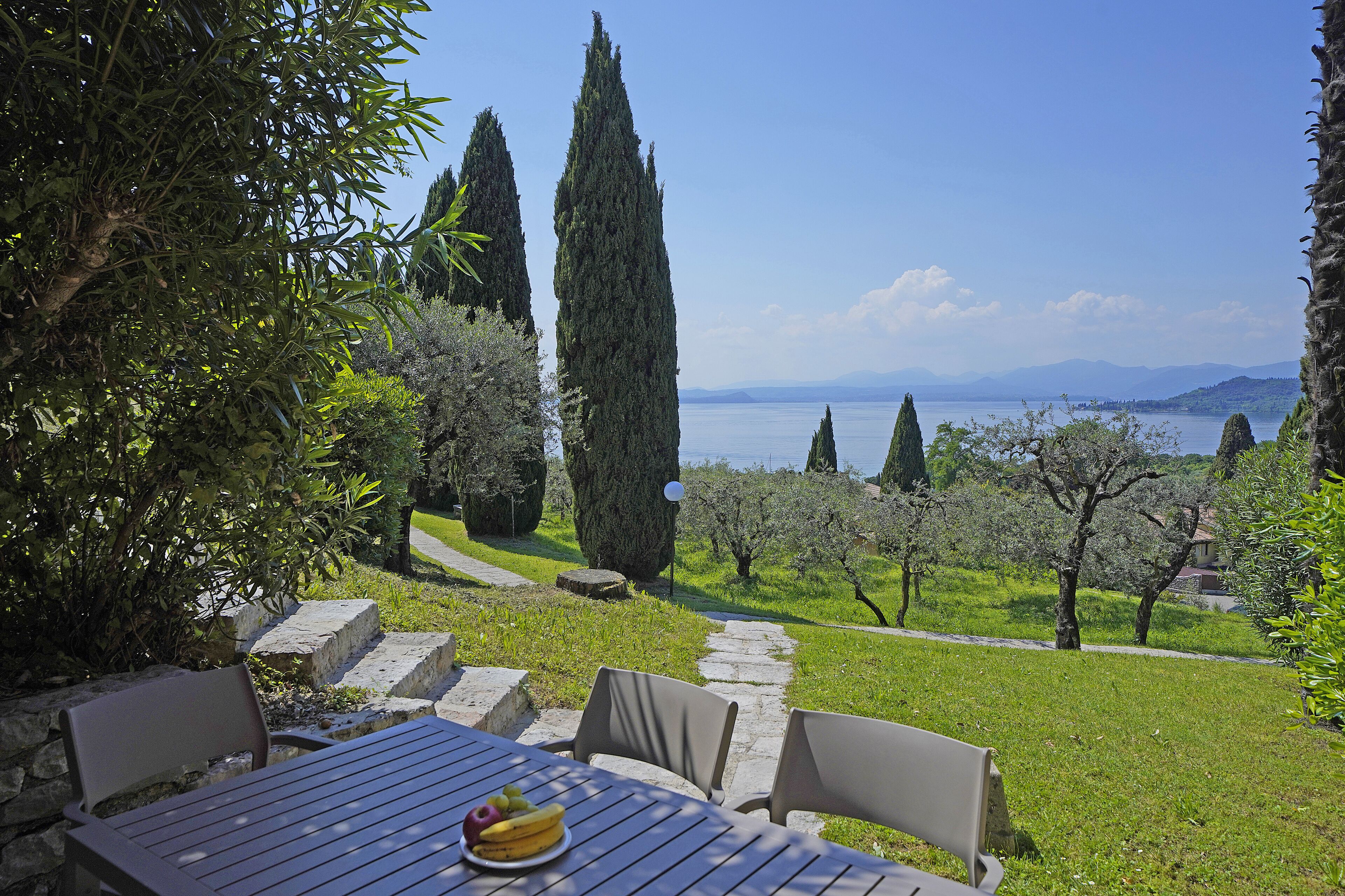 An outdoor dining area with a table and chairs, overlooking a scenic view of trees and a body of water.