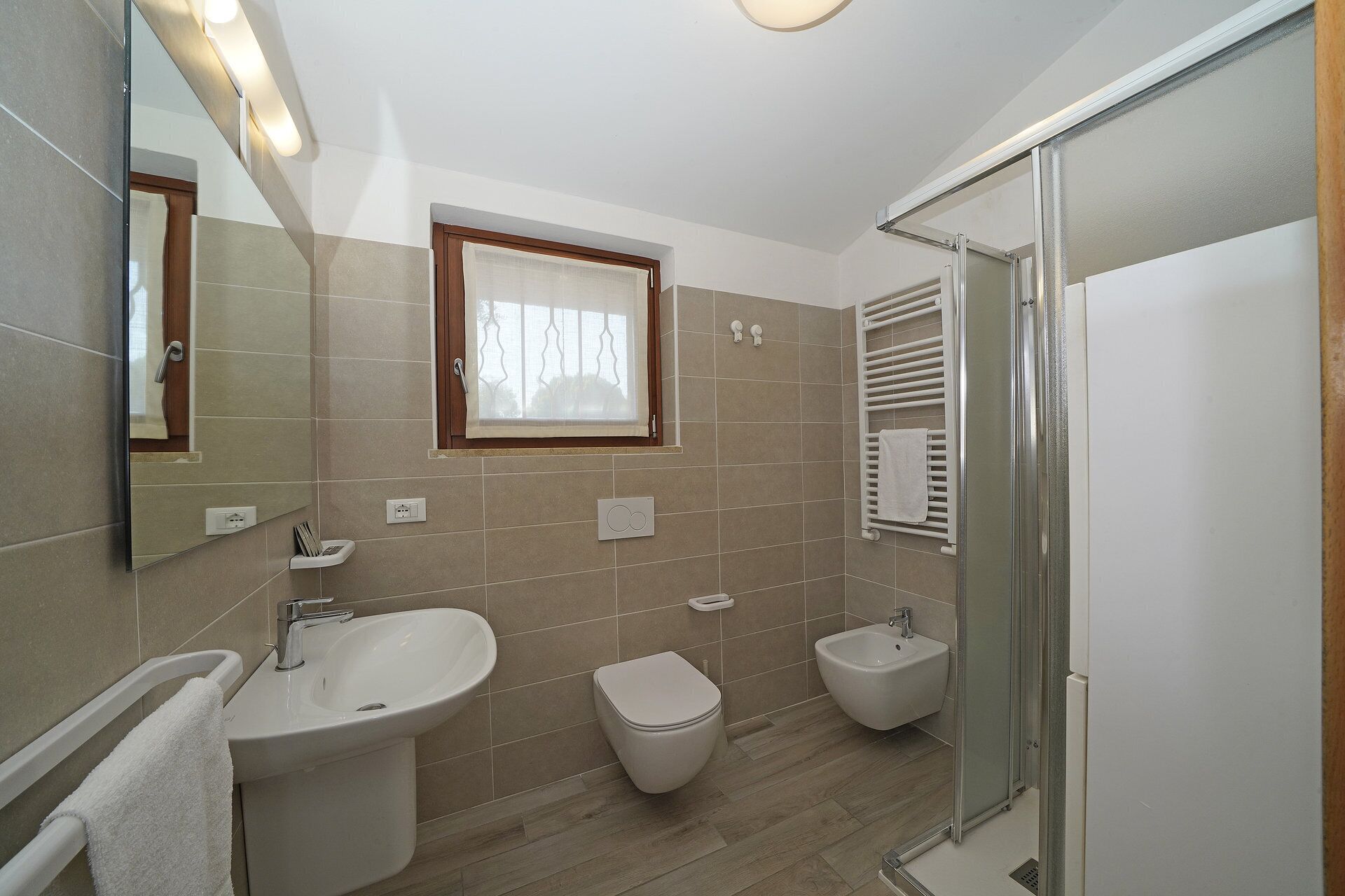 Un bagno moderno con lavandino, servizi igienici, bidet e box doccia in vetro.