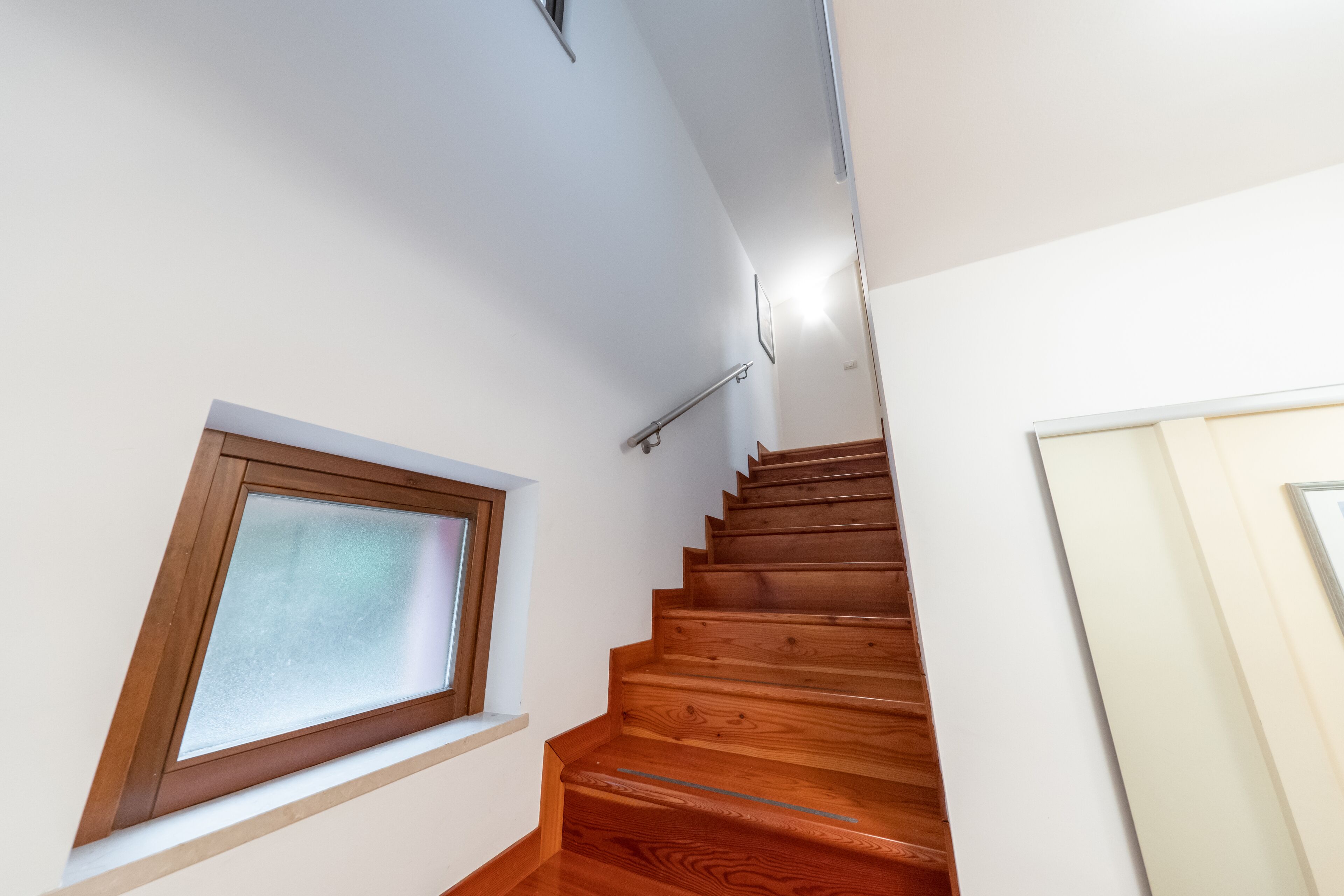 Eine Holztreppe mit Geländer, ein Fenster mit Biberglas und eine Tür auf der rechten Seite.