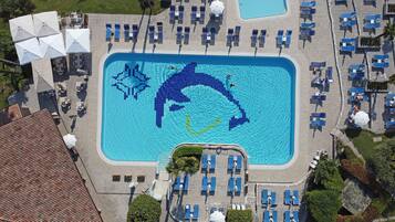 Oversigtsbillede af en swimmingpool med et delfinmosaik, omgivet af liggestole og parasoller.