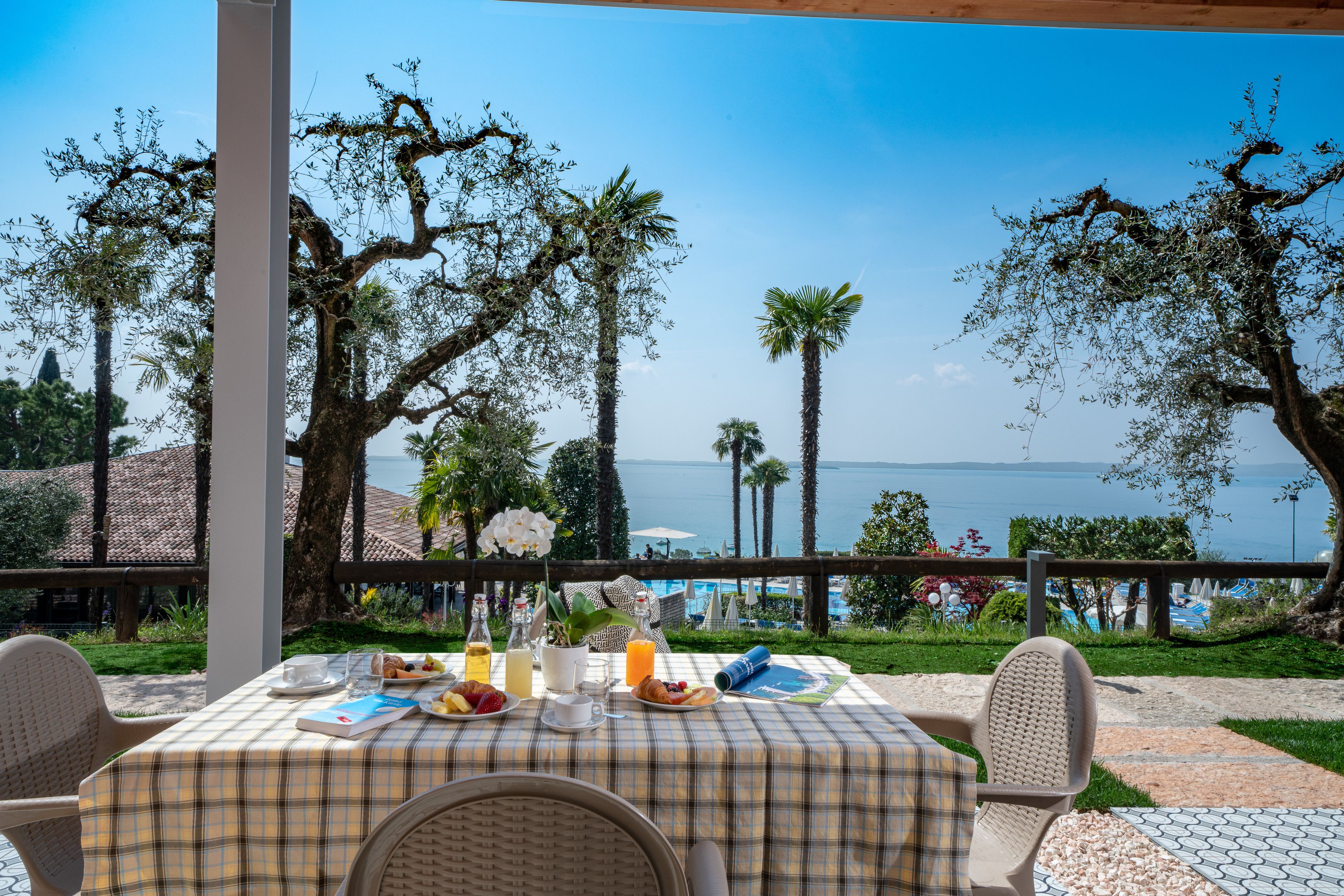 Un espace de restauration en plein air avec une table dressée pour le petit-déjeuner, offrant une vue panoramique sur la mer et les palmiers.