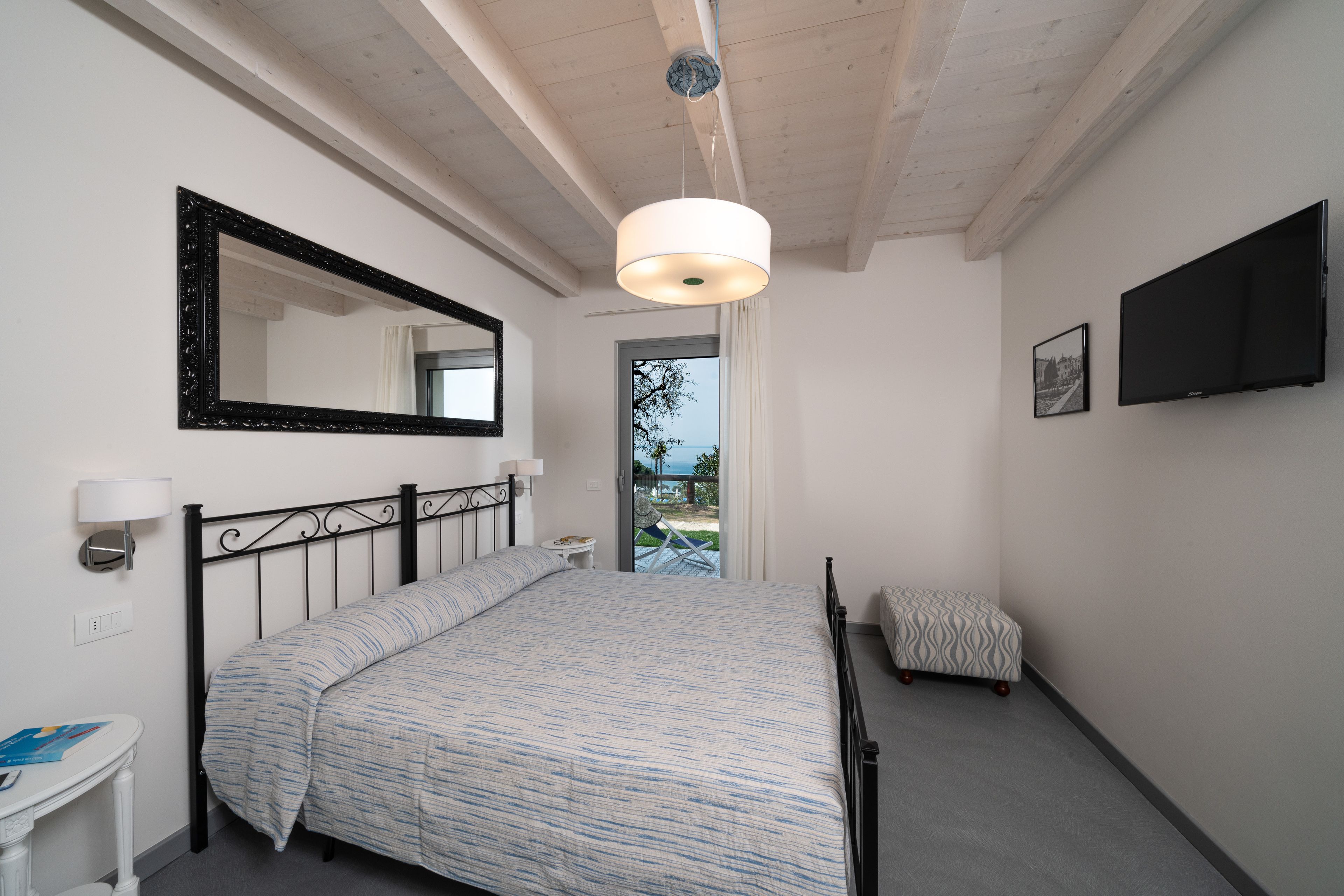 A bedroom with a bed, a bedside table, a lamp, a TV, and a view of the outdoors.