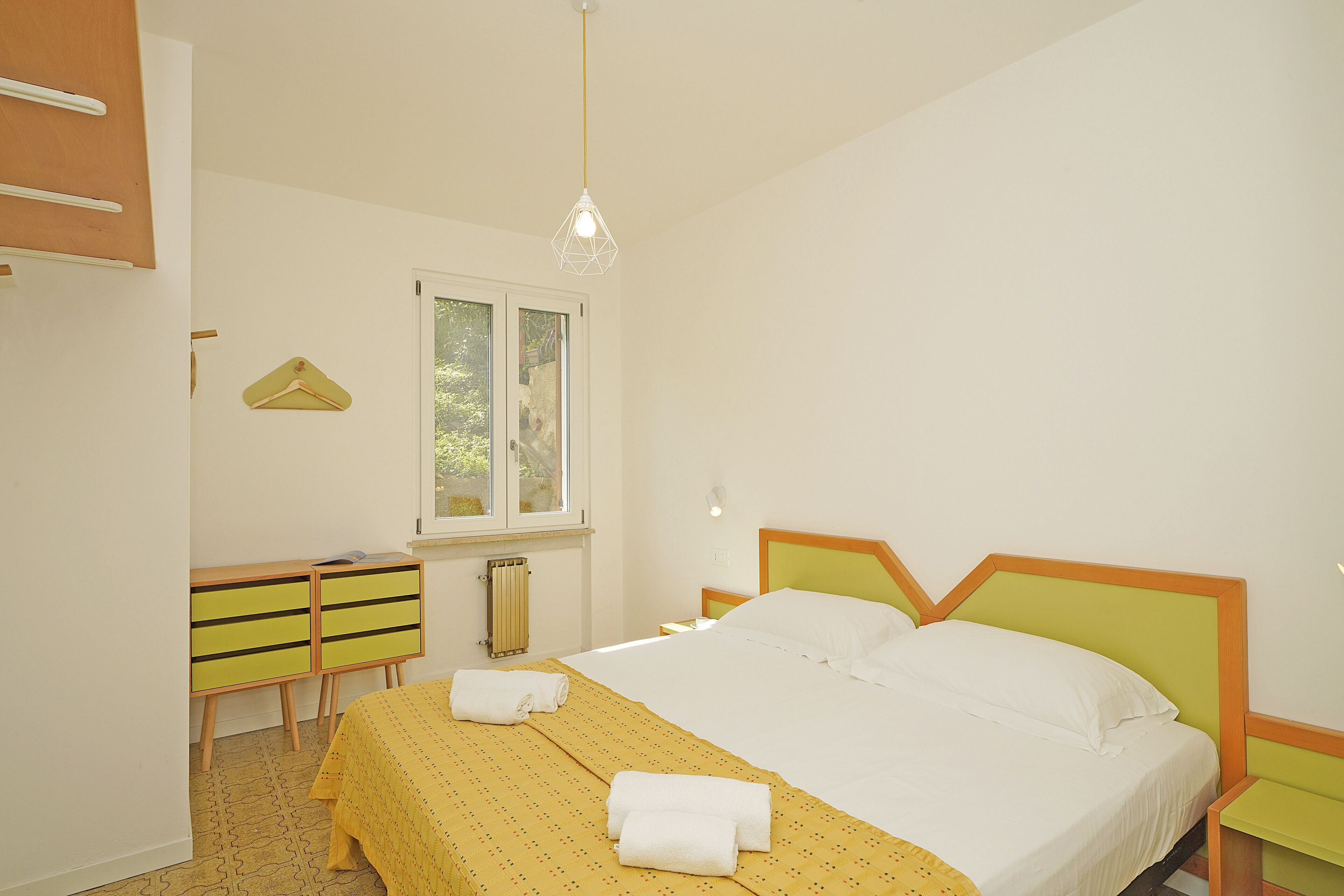 Een slaapkamer met een bed, een kaptafel, een raam en een hanglamp.