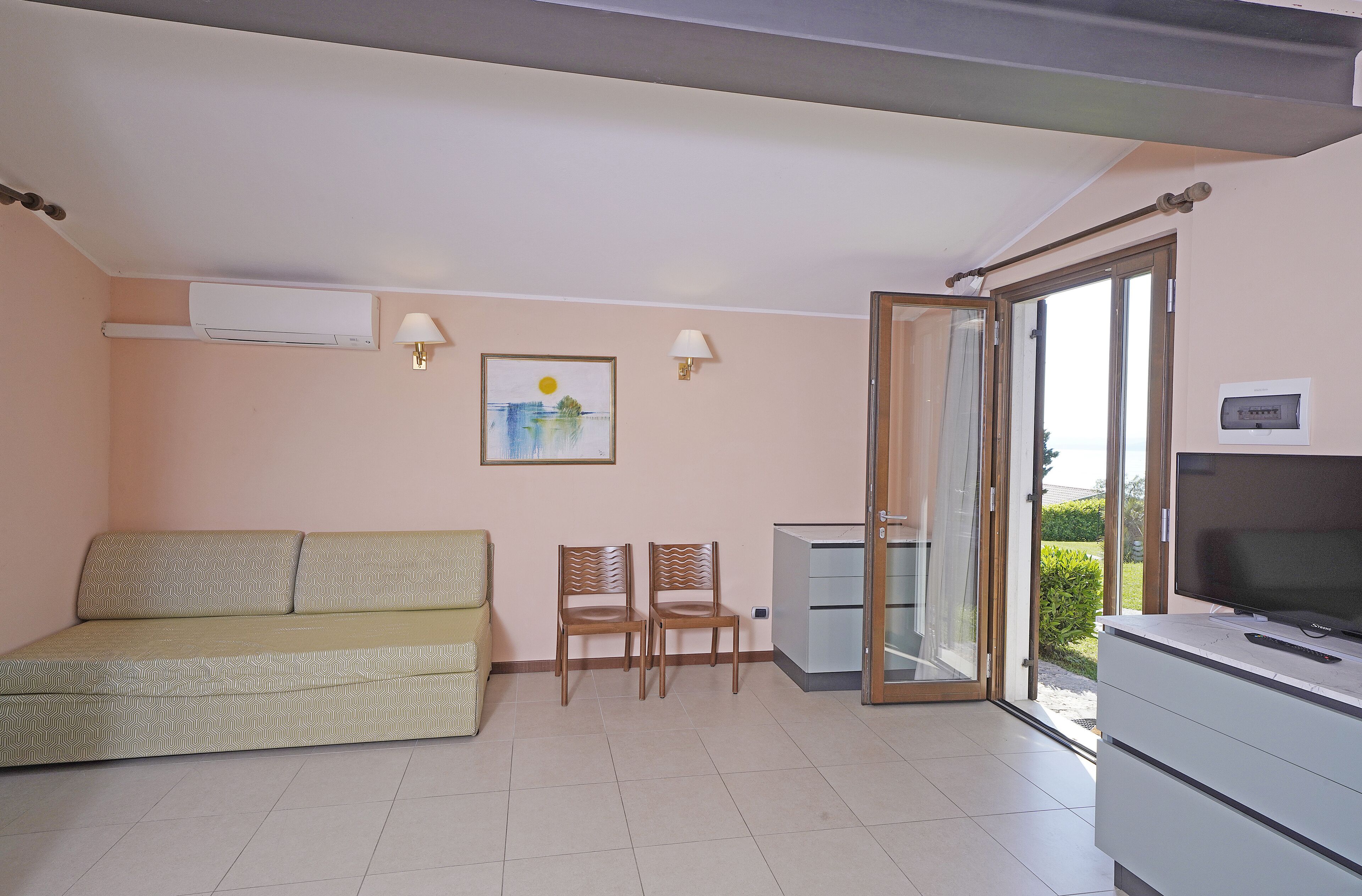 Une pièce comprenant un canapé, deux fauteuils, un bureau, un téléviseur et une porte-fenêtre coulissante donnant sur un balcon.