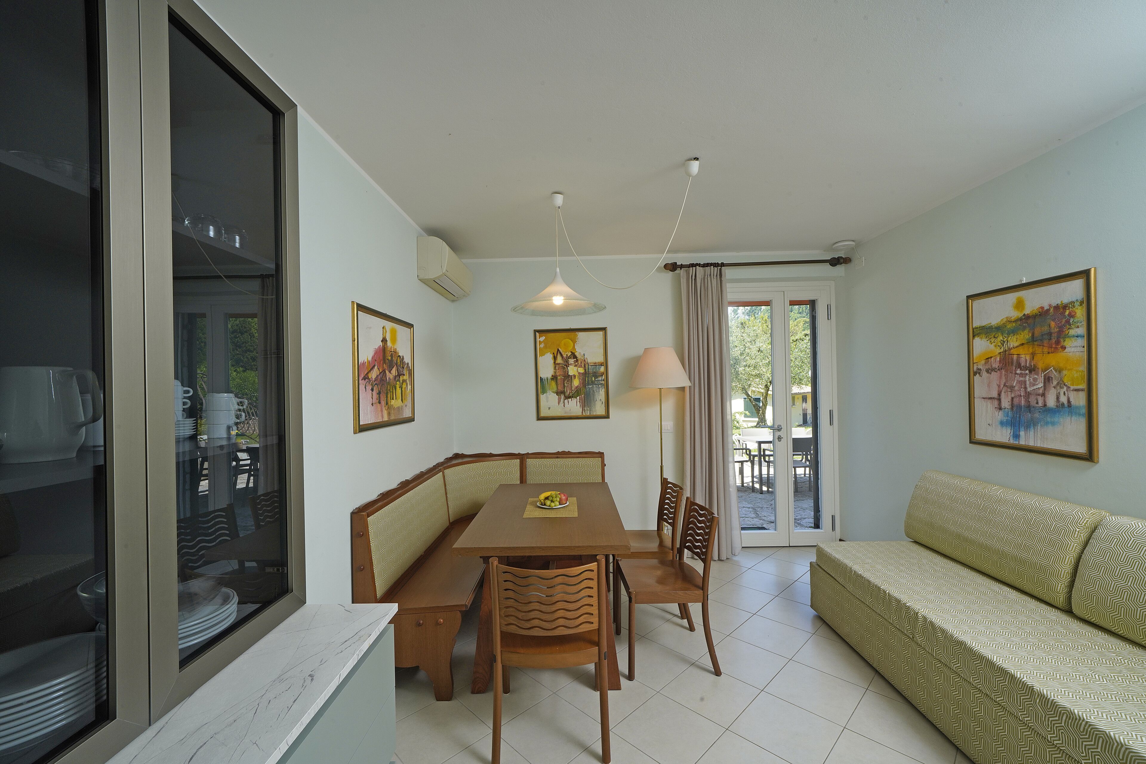 A dining area with a wooden table, chairs, and a bench. There is a sofa and a lamp in the room.
