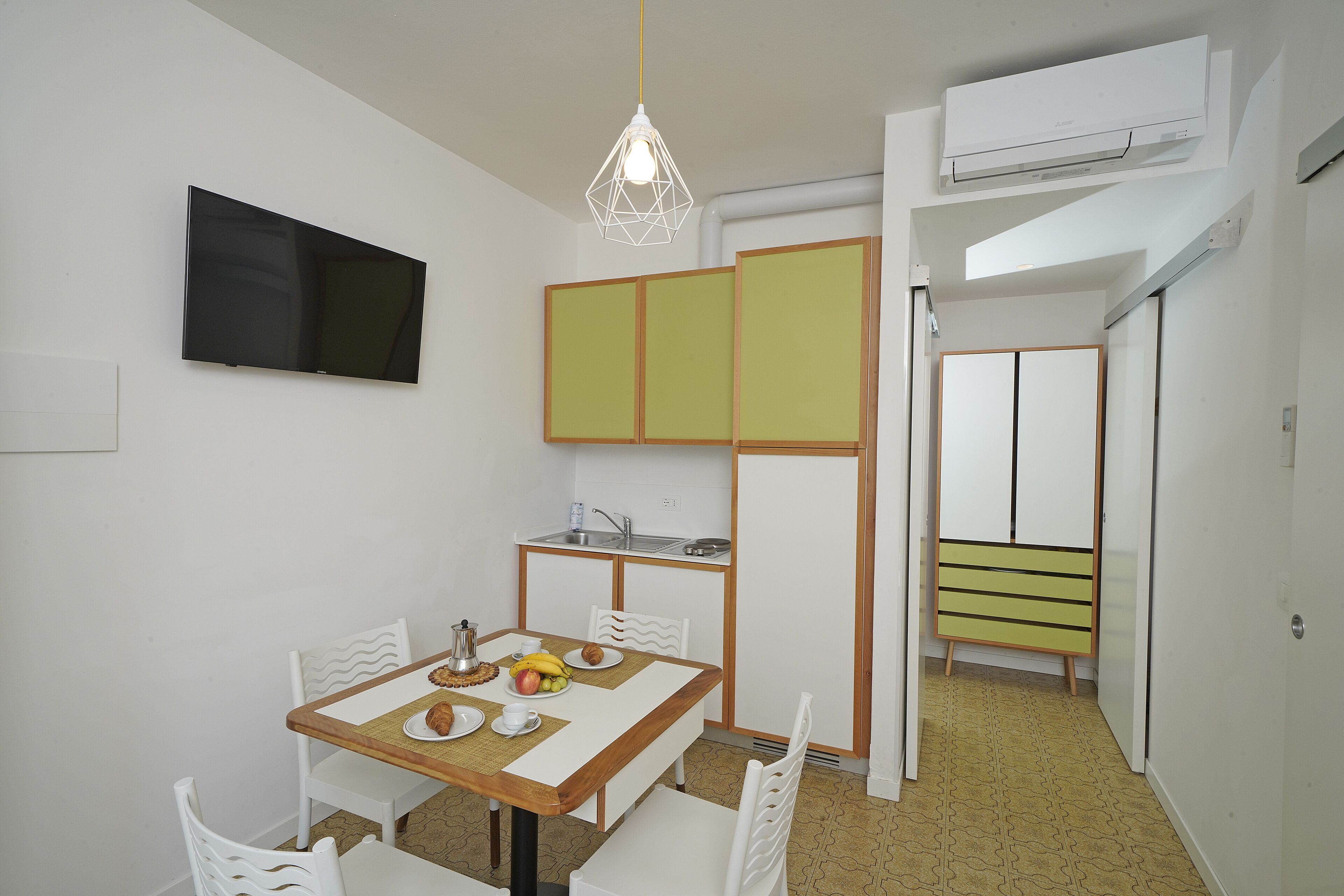 A compact kitchen with a dining area, a TV mounted on the wall, and a kitchenette.