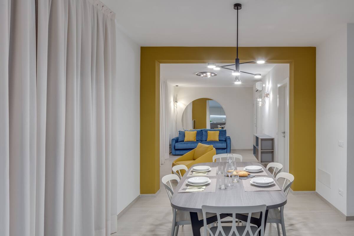 Un coin repas avec une table dressée pour quatre personnes, un canapé bleu en arrière-plan et un mur d’accent jaune.