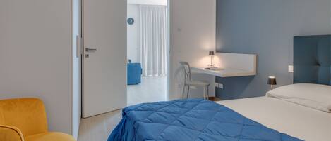 A hotel room with a bed, a desk, a chair, and an air conditioning unit.