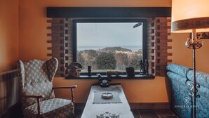 A cozy room with a view of a hilly landscape through a window with a brick frame. There is a chair, a blue sofa, and a table with a lamp. - Paraje del Asturcón Adults Only (Ribadesella)