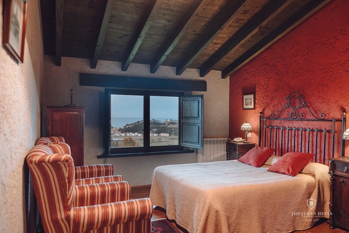 A bedroom with a bed, a window with a view, a chair, and a nightstand.