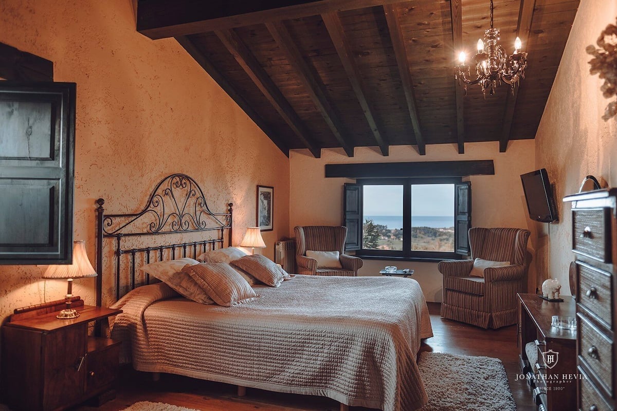 A bedroom with a large bed, a wooden ceiling, a view of the sea, and a television on the wall.