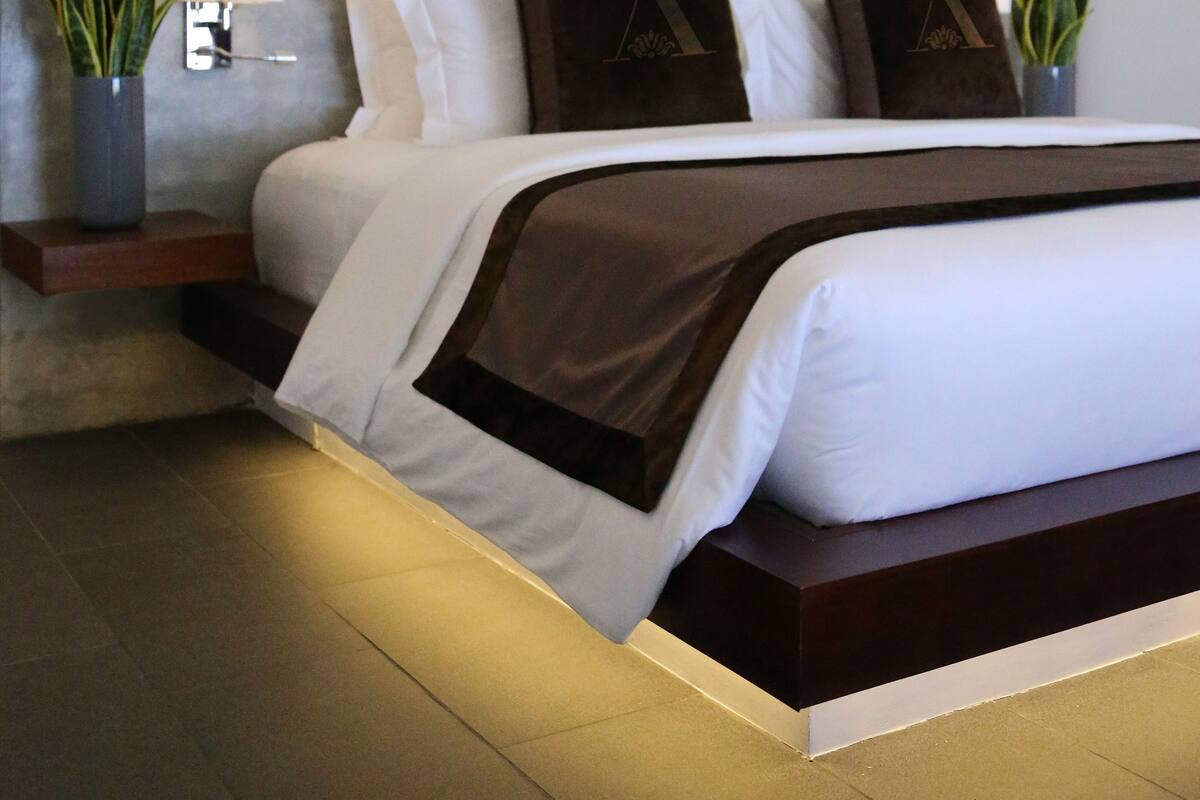 A modern hotel room with a large bed, a bedside table with a lamp, and a potted plant.
