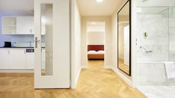 A modern hotel room with a wooden floor, a glass shower, and a bed with a red headboard.