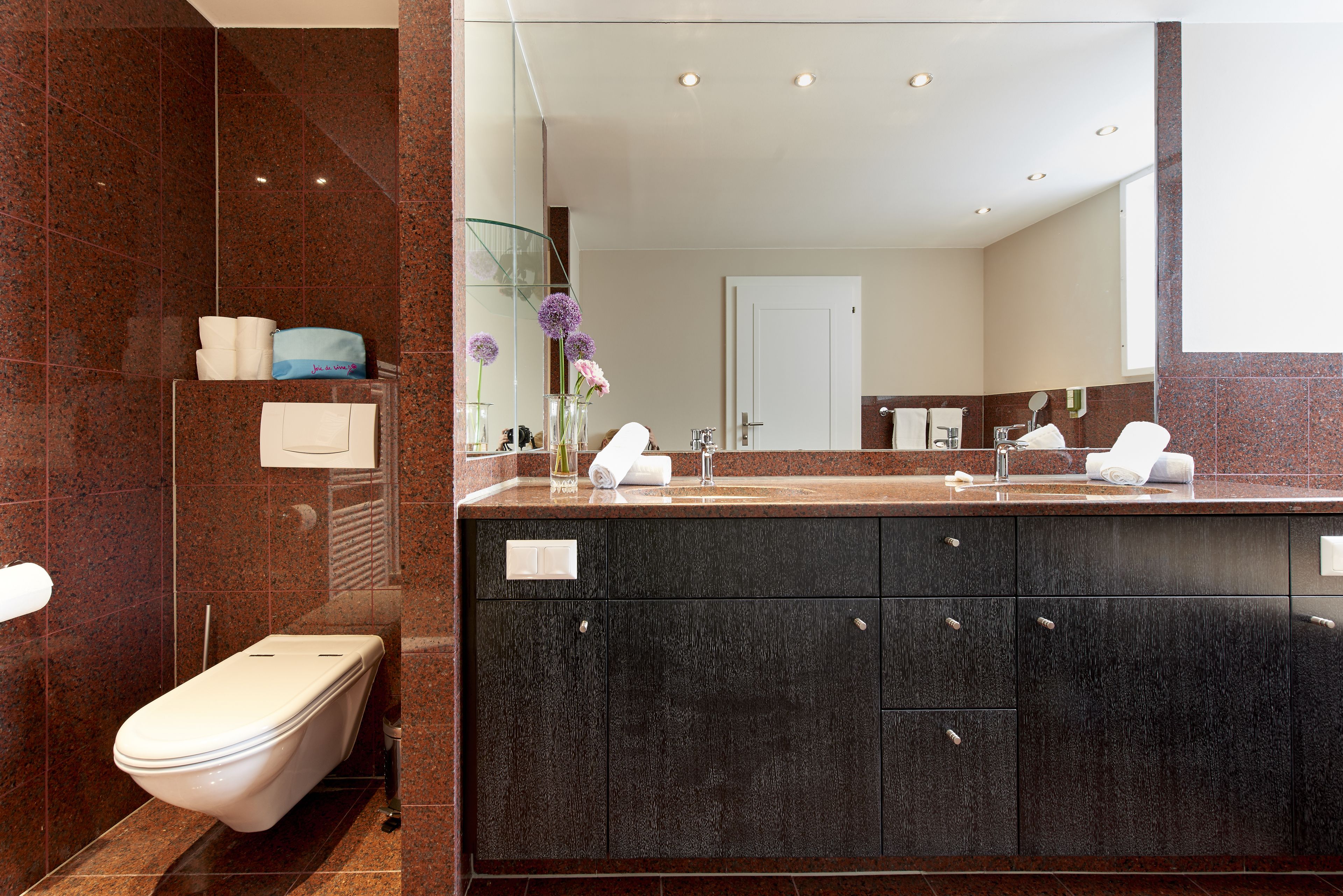 Un baño moderno con lavamanos de mármol, armarios oscuros y cabina de ducha de vidrio.