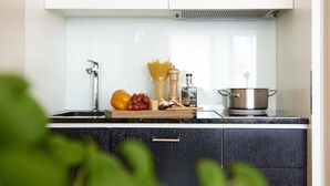 Una cocina moderna con un lavamanos de acero inoxidable, una tabla de madera con verduras, una olla en la estufa y un salpicadero blanco.