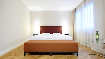 A hotel room with a bed, a nightstand, a glass table with a bottle, and a window with curtains.