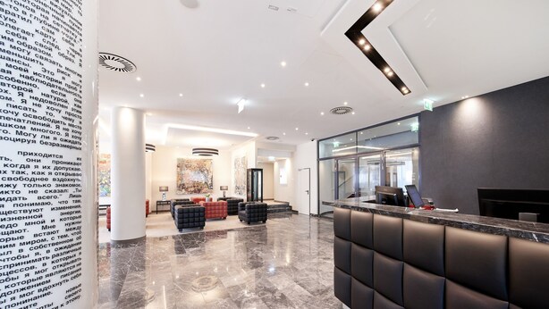 Un lobby moderno de hotel con un mostrador de recepción, área de descanso y un cuadro abstracto grande en la pared.