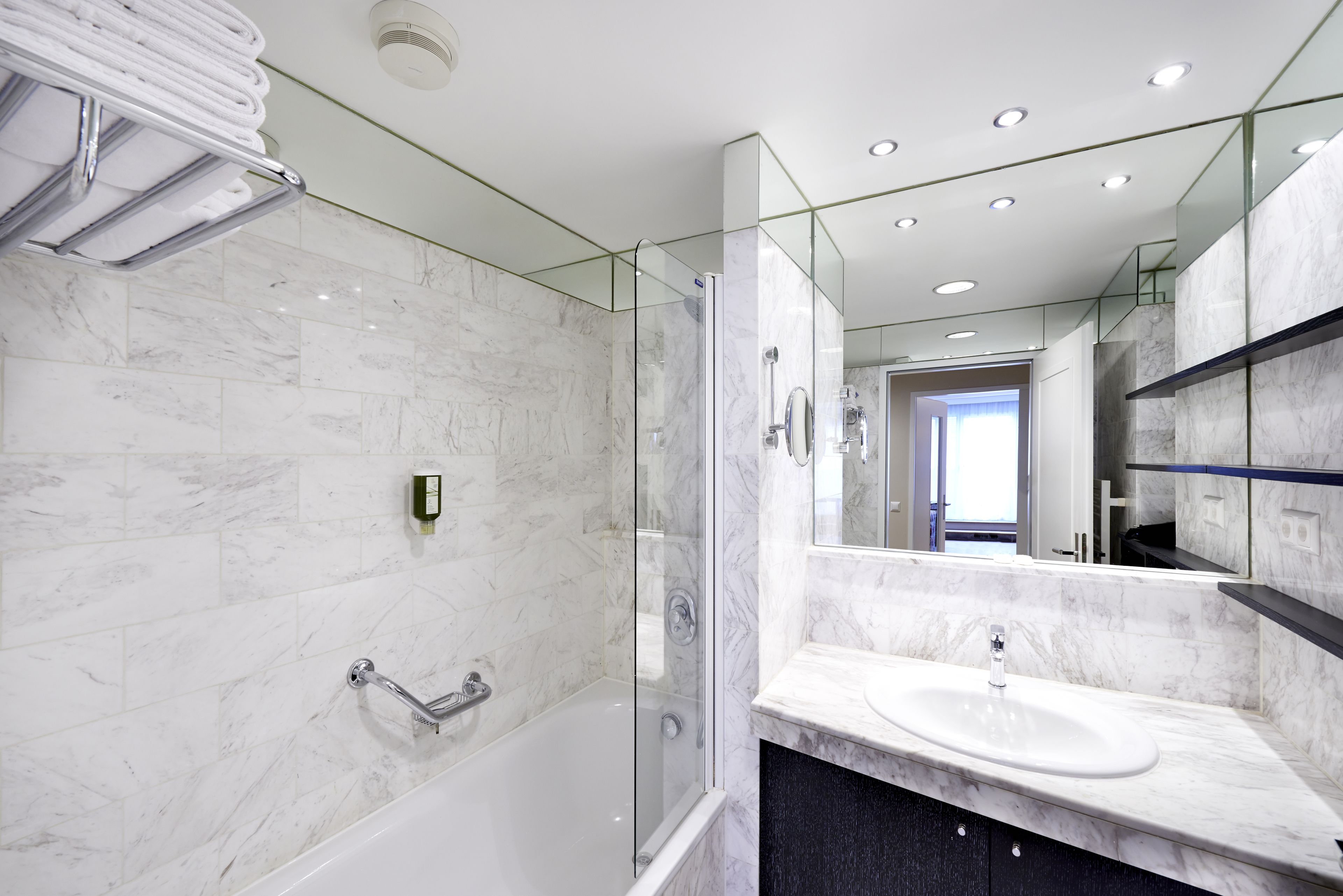 Un baño moderno con ducha de vidrio, bañera blanca y encimera de mármol con lavabo.