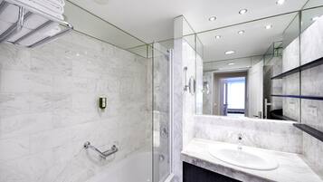 Un baño moderno con ducha de vidrio, bañera blanca y encimera de mármol con lavabo.