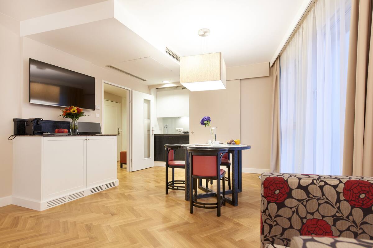 Eine moderne Küche mit weißen Schränken, ein Essbereich mit Tisch und Stühlen sowie ein an der Wand montierter Fernseher.