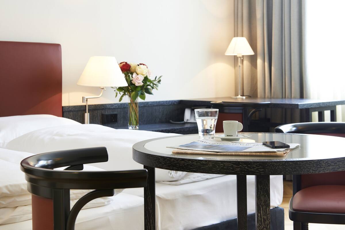 Ein Hotelzimmer mit einem Bett, einem runden Tisch mit Stuhl, einer Vase mit Blumen und zwei Lampen.