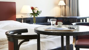Habitación de hotel con una cama, una mesa redonda con una silla, un florero con flores y dos lámparas.