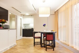 Uma cozinha moderna com armários brancos, um espaço de jantar com mesa e cadeiras, e vista da cidade através de cortinas leves.