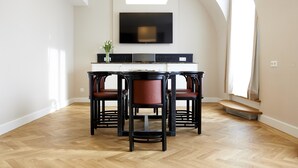 Un comedor con una mesa y sillas negras, un televisor de pantalla plana montado en la pared, y piso de madera.