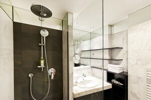 Uma casa de banho moderna com cabine de duche em vidro, lavatório de mármore e espelho com prateleiras para toalhas.