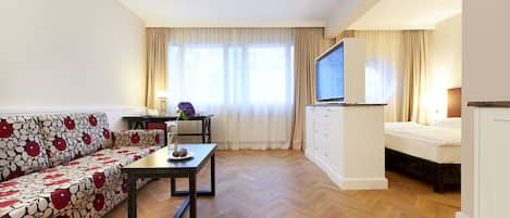 A modern hotel room with a sofa, a dining table, a TV, and a bed.