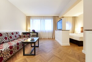 A modern hotel room with a sofa, a dining table, a TV, and a bed.