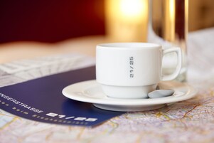Een witte mok met “21/25” erop, op een schoteltje, geplaatst op een tafel met een kaart en een boekje.