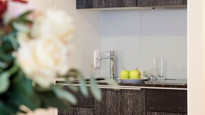 Una cocina moderna con armarios de madera oscura, un grifo de acero inoxidable y un salpicadero blanco. Hay dos manzanas verdes en la encimera y dos vasos transparentes.