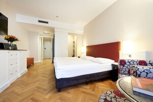 Quarto de hotel com uma cama, uma escrivaninha, uma cadeira e uma televisão.
