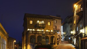 A narrow street at night with buildings on either side, featuring balconies and arched doorways. - Titano Suites (San Marino)