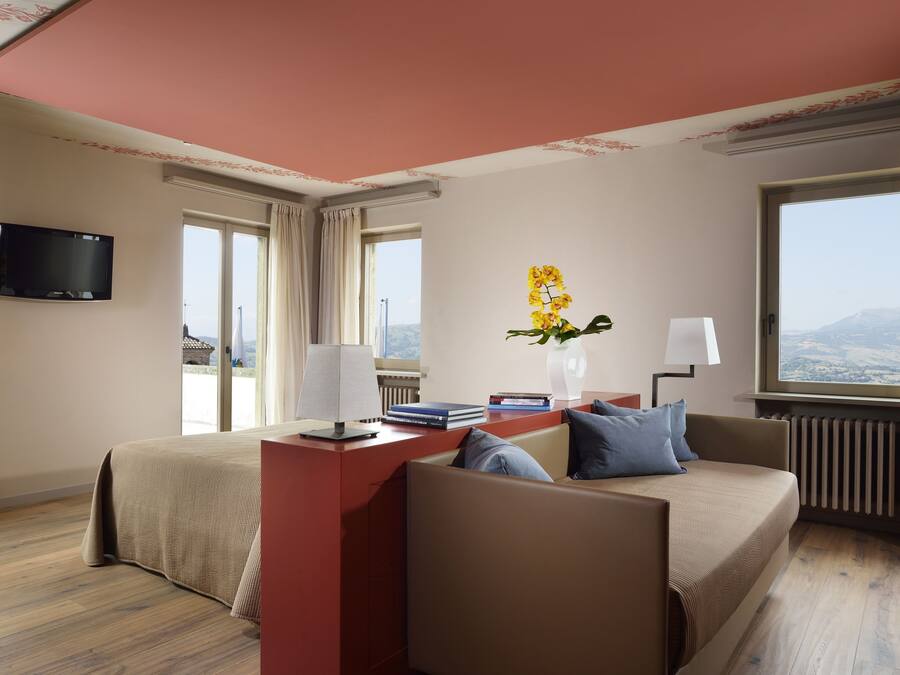 A hotel room with a bed, a sofa, a desk with a lamp, a TV, and a window with a view.