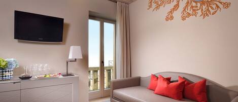 A modern living room with a flat-screen TV, a sofa with red cushions, a dining area with a vase and glasses, and a balcony with a view.