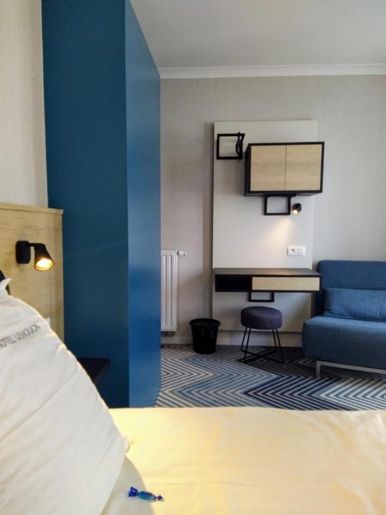 A hotel room with a bed, a desk with a chair, and a blue sofa.