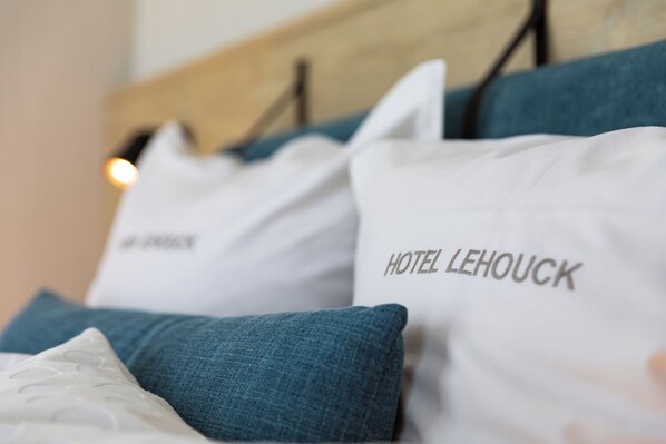 Una cama con almohadas que dicen "HOTEL LEHOUCK" y una almohada blanca con un logotipo.