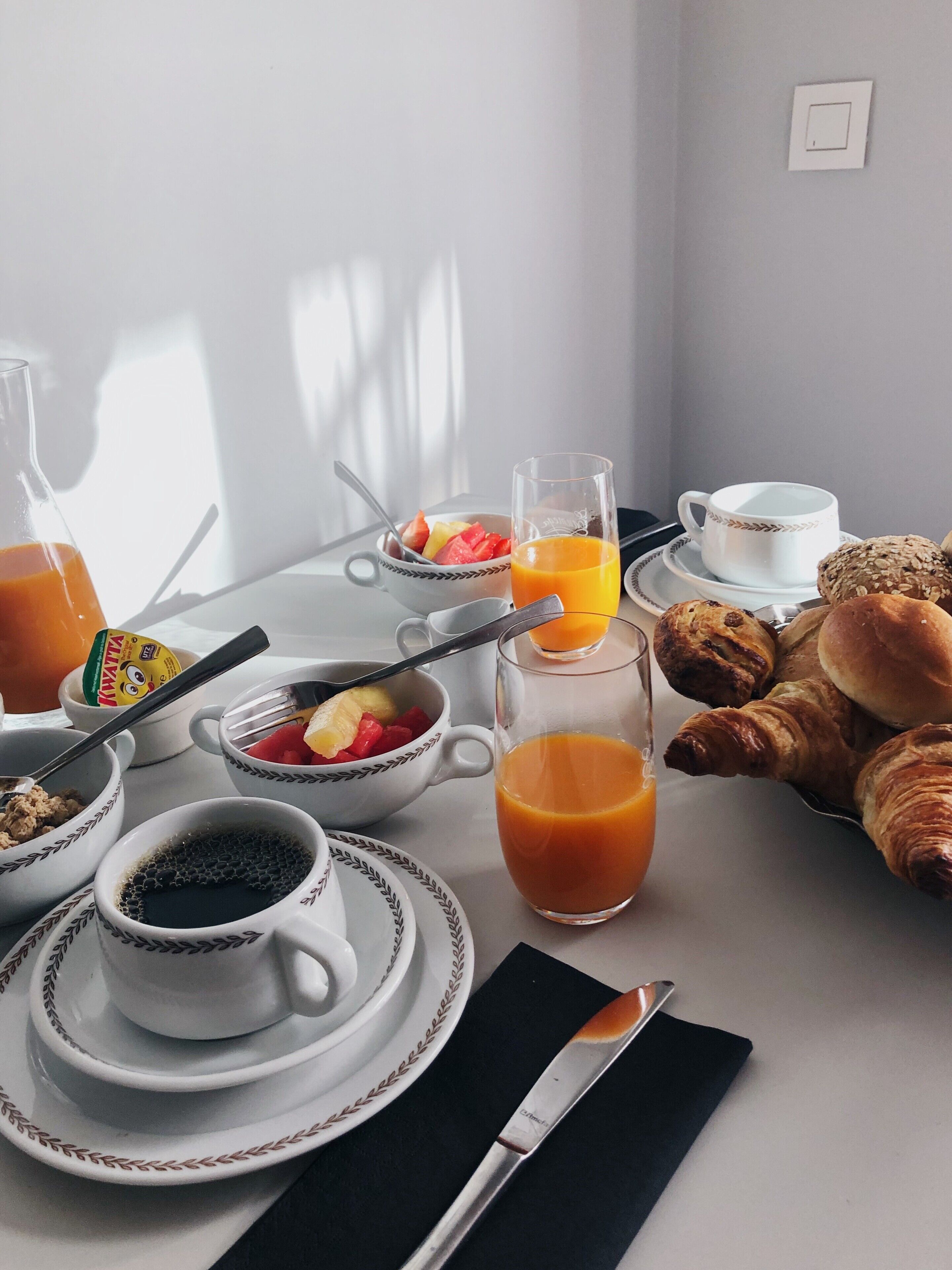 Una mesa de desayuno con tazones de cereal, un vaso de jugo de naranja, croissants y una taza de café.