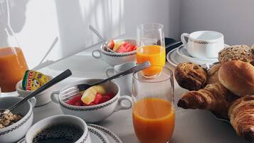 Una mesa de desayuno con tazones de cereal, un vaso de jugo de naranja, croissants y una taza de café.