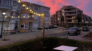 Vista da rua ao entardecer, com edifícios, postes de luz e luzes de Natal.