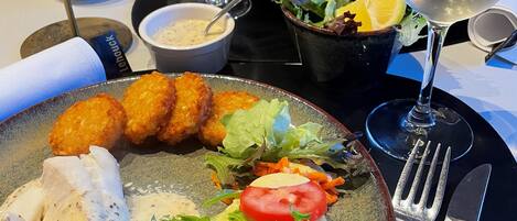 A dining table with a plate of food, including fish, salad, and bread rolls, and two glasses of white wine.